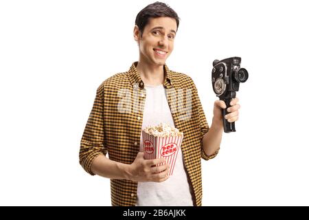 Guy lächelt und hält eine 8-mm-Vintage-Kamera und eine Schachtel Popcorn, die auf weißem Hintergrund isoliert sind Stockfoto