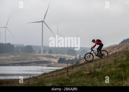 Zwei Männer fahren Mountainbikes im Schatten von Windkraftanlagen in der Nähe des Lluest-Wen-Reservoirs in Südwales. Stockfoto