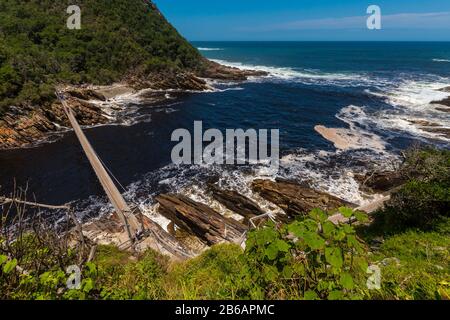 Ein weiter Blick hinunter auf Storms River Mouth, wo der Fluss auf das Meer trifft, und die Hängebrücke über den Fluss. Tsitsikampa National Park, S Stockfoto