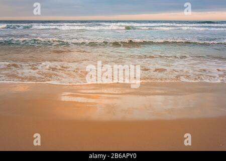 Ruhige Wellen, die am Strand der Plettenberg Bay brechen und die Farben des Sonnenuntergangs widerspiegeln. Garden Route, Westkaper, Südafrika Stockfoto