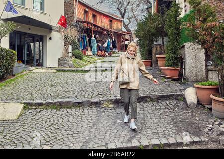 Ein junger kaukasischer weiblicher Tourist, der in der türkischen Stadt Istanbul eine Straße hinuntersteigt. Eine hübsche weiße Frau spaziert im Winter durch eine Touristenstadt. Stockfoto