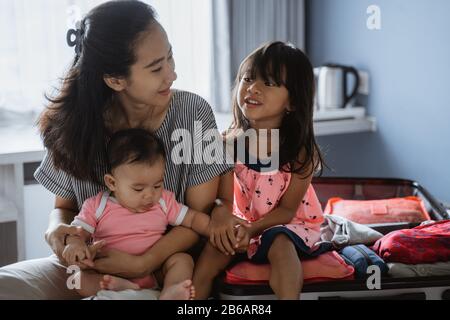 Mutter chattet mit ihren beiden Kindern, nachdem sie einen Koffer für den Urlaub vorbereitet hat Stockfoto