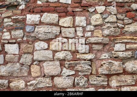 Die Beschaffenheit des Steinzauns auf Tonmörtel. Raue Kopfsteinpflasterwand, abstrakter Hintergrund. Stockfoto