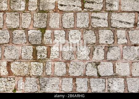 Die Wandoberfläche besteht aus grauem Kopfsteinpflaster, der mit einer Lösung aus rotem Ton befestigt ist. Textur eines Steinzauns für den Hintergrund. Stockfoto