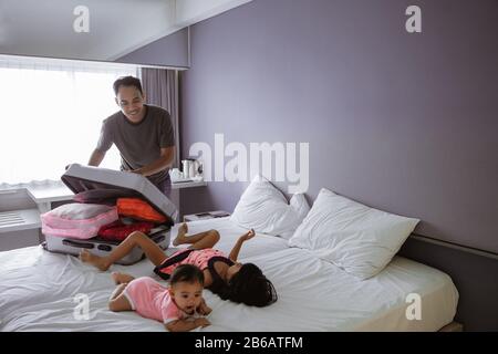 Vater bereitet den Koffer vor, als seine beiden Kinder auf dem Bett im Zimmer spielen Stockfoto