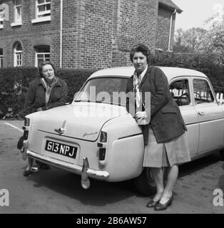 In den 1950er Jahren standen historisch zwei Damen neben ihrem Motorwagen der Epoche. Autobesitz veränderte das Leben der Weibchen, da ihnen in früheren Generationen Freiheiten unerhört wurden. Stockfoto