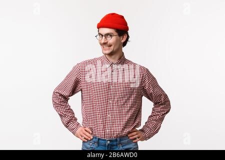 Hochkarierter Hochdruck im Taillenbereich und begeisterter junger Flusspferd in roter Mütze und Brille mit kariertem Hemd, bereit stehend mit selbstbewusster gerader Pose Stockfoto