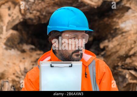 Forsttechniker, der mit einem Notizblock in der Zwischenablage neben einem Baumlogan in der Walde posiert, ist zuversichtlich, dass männliche Fachmann Daten auf dem Feld sammelt Stockfoto