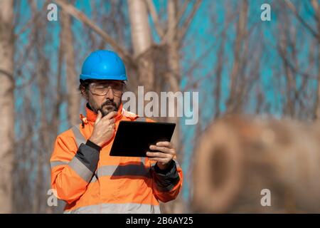 Forsttechniker, der einen digitalen Tablet-Computer in der Waldstruktur verwendet, um während der Entwaldung Daten zu erfassen Stockfoto