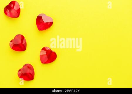 Herzförmige rote Kristalle auf gelbem Hintergrund. Knusprige Herzen auf der Oberseite. Ansicht von oben. Das Konzept der Wiederholung. St. Valentine's D Stockfoto