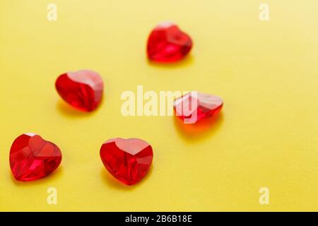 Herzförmige rote Kristalle auf gelbem Hintergrund. Knusprige Herzen auf der Oberseite. Ansicht von oben. Das Konzept der Wiederholung. St. Valentine's D Stockfoto