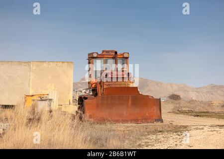 Der alte verlassene verrostende Traktor auf der Straße. Stockfoto