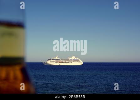 Corona-Bierflasche verschwimmen mit einem Kreuzfahrtschiff am Meer in der Nähe von Giardini Naxos, Sizilien, Italien. Stockfoto