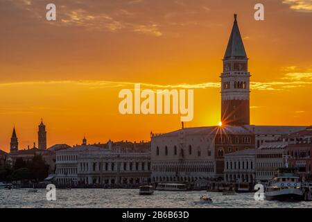 Farbenfroher Sonnenuntergang über dem historischen Zentrum von Venedig, Italien, mit Sonnenstrahlen, die vom Campanile di San Marco über dem Dogenpalast gefiltert werden Stockfoto