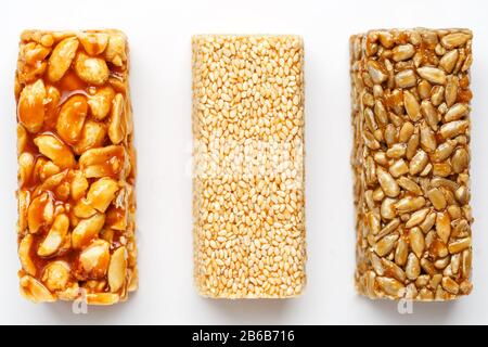 Korngranola-Leiste mit Erdnüssen, Sesam und Samen in einer Reihe auf weißem Grund. Draufsicht Drei verschiedene Balken, isolieren Stockfoto