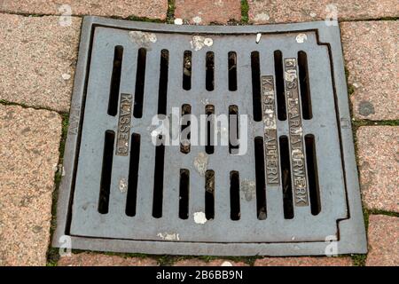 Mit Kopfsteinpflaster ummauerte Mannhole-Abdeckung auf der Straße Stockfoto
