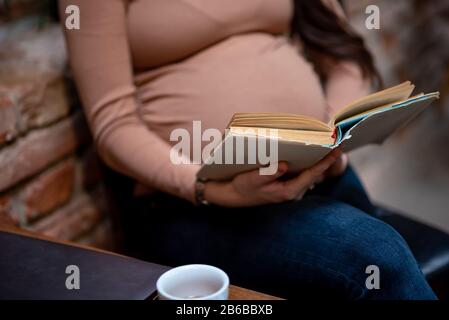 Schwangere Frau liest das alte Buch im Café Stockfoto