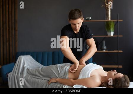 Junge schöne Frau, die im Spa eine Antikellulit-Bauchmassage genießt.professionelle Massagetherapeutin behandelt eine Patientin in der Wohnung.Entspannung Stockfoto