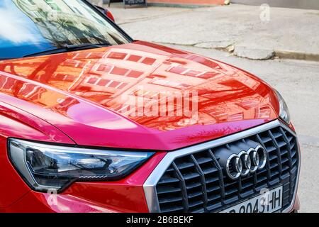 Varna, Bulgarien, 28. Dezember 2019. Audi Autogitter mit Chrom-Logo und Fronthaube mit Reflexionen von Wohnhäusern. Rotes Auto geparkt auf Stree Stockfoto