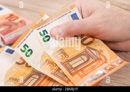 Die Hand eines Mannes fasst zwei 50 Euro-Scheine. Im Hintergrund liegen Euro-Banknoten auf dem Tisch. Stockfoto