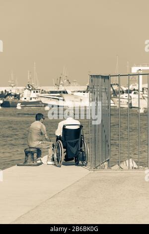 LLORET DE MAR, SPANIEN - 8. AUGUST 2019: An einem Sommertag sitzen zwei Männer am Rande des Piers. Stockfoto