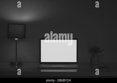 Dunkler Schreibtisch in der Nacht, beleuchtet von einer Lampe und einem Laptop-Bildschirm. Sauberer moderner Arbeitsplatz für Telearbeit oder freiberufliche Tätigkeit, niedrige Grundstimmung Stockfoto
