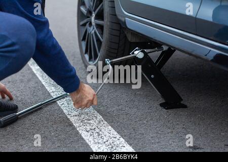 Nahaufnahme der Reparatur eines flachen Reifens. Der Mann hebt ein Auto mit einem Wagenheber für den Radwechsel, Prag, März 2020. Stockfoto