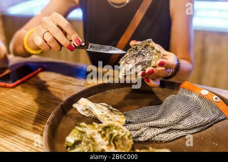 Frau öffnet im Restaurant eine Auster mit Messer Stockfoto