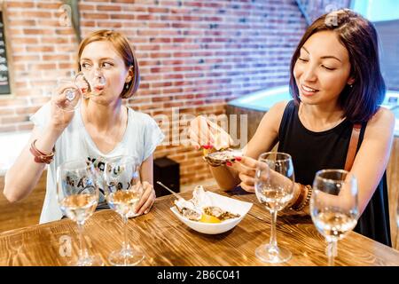 Zwei weibliche Freunde in einem Restaurant, die Austern und Schalentiere essen und Weißwein trinken Stockfoto