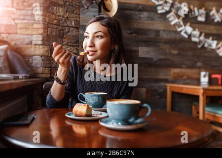 Schöne junge asiatin, die in einem Café sitzt und leckeren Kuchen isst Stockfoto