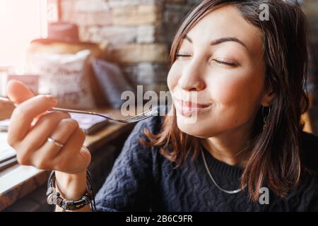 Schöne junge asiatin, die in einem Café sitzt und leckeren Kuchen isst Stockfoto