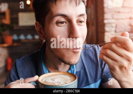 Junger Mann, der Kaffee mit Kuchen im Café genießt Stockfoto