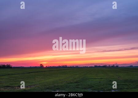 Wunderschöner Sonnenuntergang mit einem bunten Himmel über einer holländischen Landwirtschaftspolderlandschaft in der Nähe der Stadt Delft und in der Nähe von Rotterdam, Niederlande Stockfoto