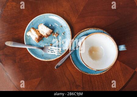 Die Überreste von Essen auf dem Tisch im Café, flacher Blick. Becher mit Kaffee und Gabel mit einem Teller mit Krümel aus einem Käsekuchen Stockfoto