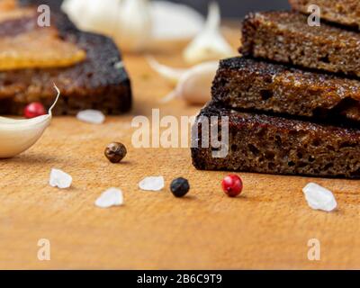 Ein Laib aus hausgemachtem Roggenbrot liegt auf einer Holztafel, die von Knoblauch und Gewürzen umgeben ist Stockfoto