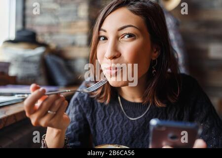 Schöne junge asiatin, die in einem Café sitzt und leckeren Kuchen isst Stockfoto