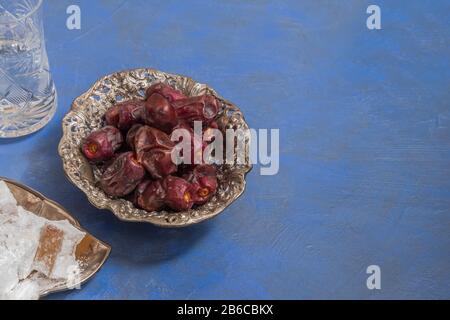 Ramadan Food and Drinks Konzept. Trockendaten, lokum und ein Glas Wasser auf blauem Hintergrund mit Kopierraum Stockfoto