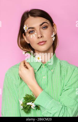 Schöne junge Frau mit Blumen im Gesicht und im Ärmel auf pinkfarbenem Hintergrund. Federkonzept. Stockfoto