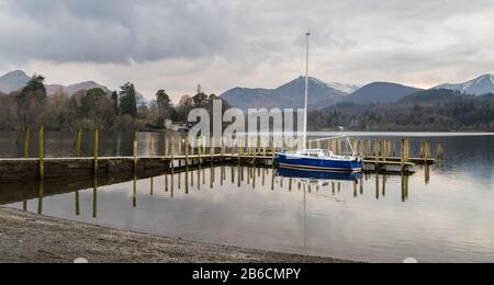 Ein blaues und weißes Segelboot, das im März 2020 auf einem Steg auf Derwent Water in Cumbria festgemacht wurde. Stockfoto