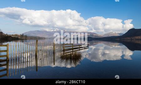 Ein mehrbildliches Panorama von Holzzäunen, das in Derwent Wasser mit Skiddaw in der Ferne reflektiert. Stockfoto