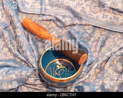 Haulerwijk - 07. märz 2020: Haulerwijk, Niederlande. Blaue und goldene Gesangsschüssel aus sieben Metallen mit einem Holzstreifer auf einem indischen Schal Stockfoto