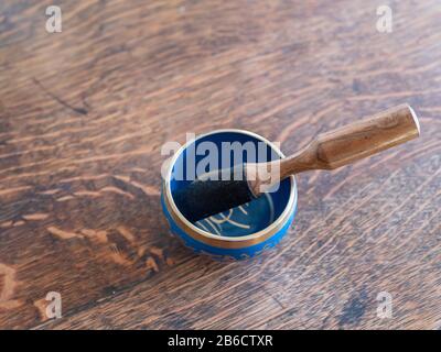 Haulerwijk - 07. März 2020: Haulerwijk, Niederlande. Blaue und goldene indische Gesangsschüssel aus sieben Metallen mit einem Holzstreifer auf einem Holz Stockfoto