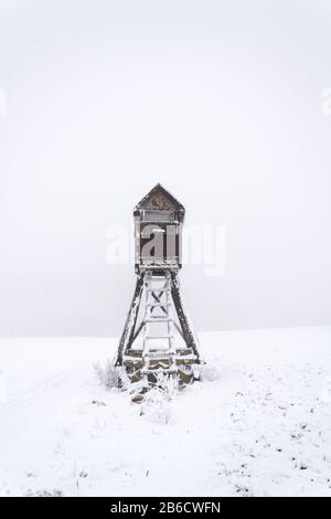 Hirschstand, Holzjäger hoher Sitz verstecken sich auf schneebedecktem Feld, Winterfoggy Day Stockfoto