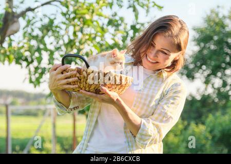 Reife lächelnde glückliche Frau, die Ingwerkätzchen in den Korb hält Stockfoto