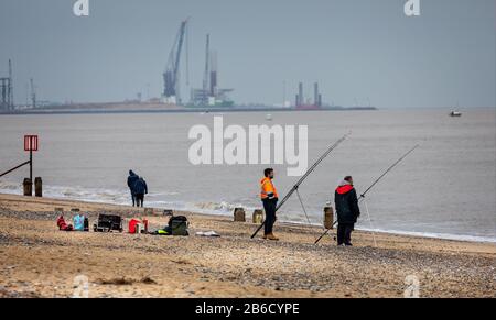 Fischer, die am 7. März 2020 mit Kränen im Yarmouth Harbour im Hintergrund in der Nähe von Lowestoft, Norfolk, Großbritannien, vor dem Strand angeln Stockfoto