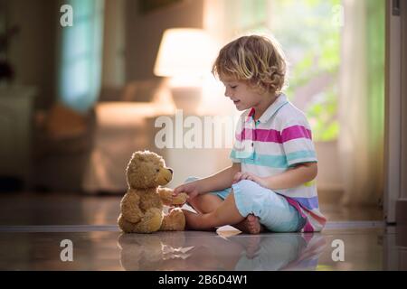 Kind, das mit Teddybär spielt. Kleiner Junge umarmt sein Lieblingsspielzeug. Kind und gestopftes Tier zu Hause. Kleinkind sitzt auf dem Boden des Wohnzimmers mit B. Stockfoto