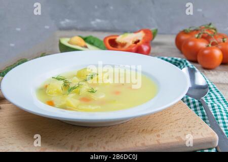 Weiße Milchsuppe mit Kartoffeln, Karotten, Grüns steht in einem weißen Teller auf einem Holzbrett Stockfoto