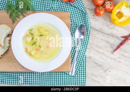 Weiße Milchsuppe mit Kartoffeln, Karotten, Grüns steht in einem weißen Teller auf einem Holzbrett Stockfoto