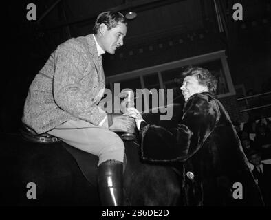 Vintage-Foto von Filmstar Errol Flynn (zwischen den Jahren von 1907 und 1959) und der US First Lady Eleanor Roosevelt (zwischen den Jahren von 1984 und 1962). Flynn wird auf einem Pferd des Weißen Hauses namens Badger abgebildet, während er im Rahmen der Geburtstagsfeierlichkeiten für Präsident Franklin D Roosevelt auf einem Hufeisen in Fort Myer, Virginia, verliehen wird. Foto von Harris & Ewing aufgenommen am 25. Januar 1939. Stockfoto