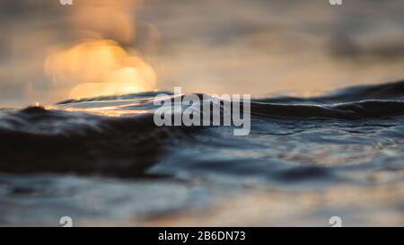 Ruhiger Sonnenuntergang am Strand an der Südsommerküste und bunte blaue kleine Welle, bokeher Hintergrund Stockfoto